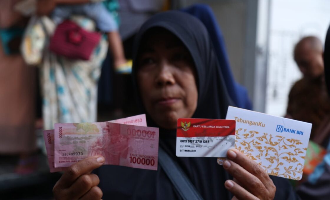 Penerima Bantuan Sosial PKH Menunjukkan Uang Tunai dan Kartu Keluarga Sejahtera