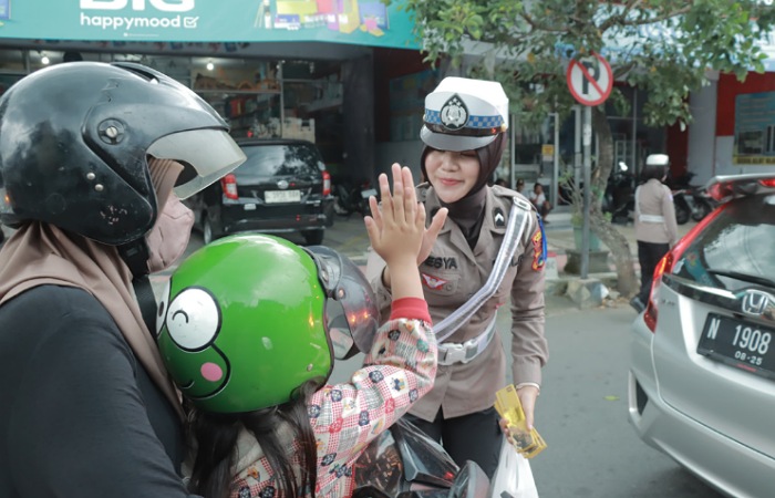 Seorang Polwan Satlantas Polres Blitar sedang nemberi reward kepada anak kecil saat ia mematuhi peraturan.