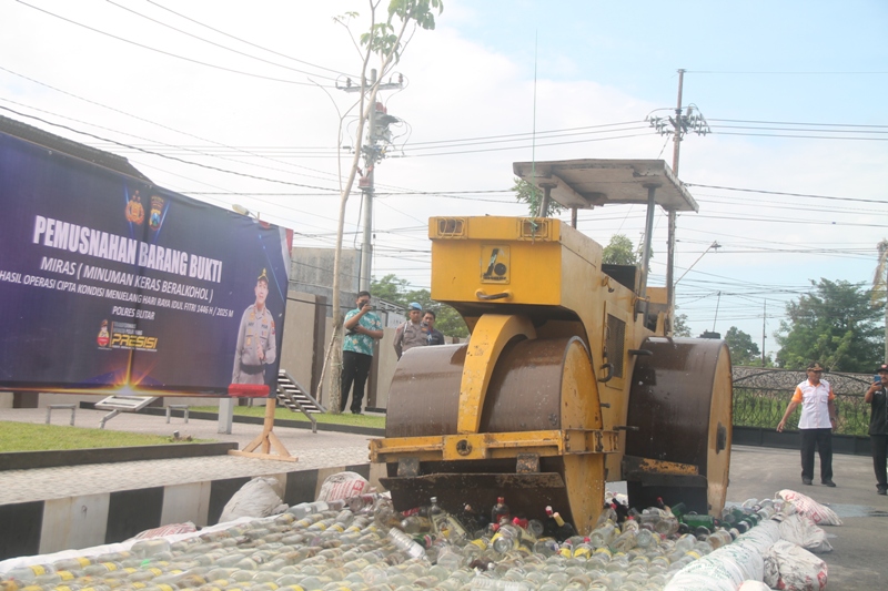 HANCUR: Alat berat sedang memusnahkan ribuan botol miras yang disita polisi dari pengedar atau penjual.