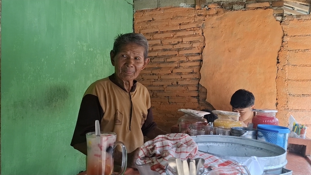 NIKMAT: Mbah Karyani  saat melayani pelanggan setia di lapak sederhananya di Kelurahan Tanggung, Kecamatan Kepanjenkidul, Kota Blitar, Jumat (18/7/2025).