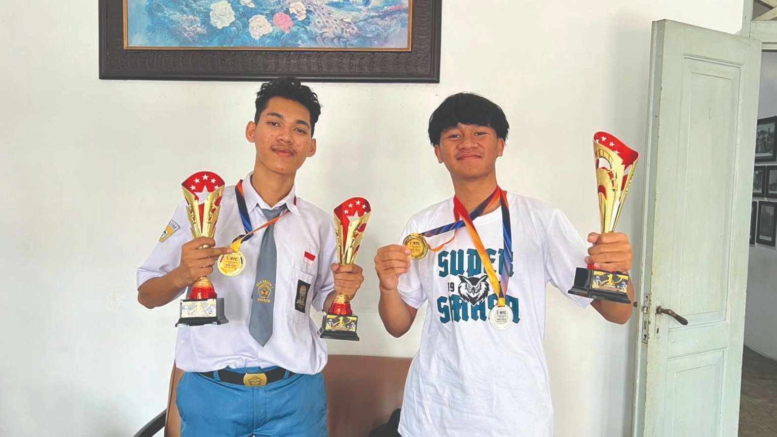 TAULADAN: Dua siswa SMA Negeri 1 Blitar, Arsyaka Kheyza dan Erga Raditya dengan medali emas dan piala yang diraih dalam Kompetisi Robotik Internasional 2025 di Malaysia.