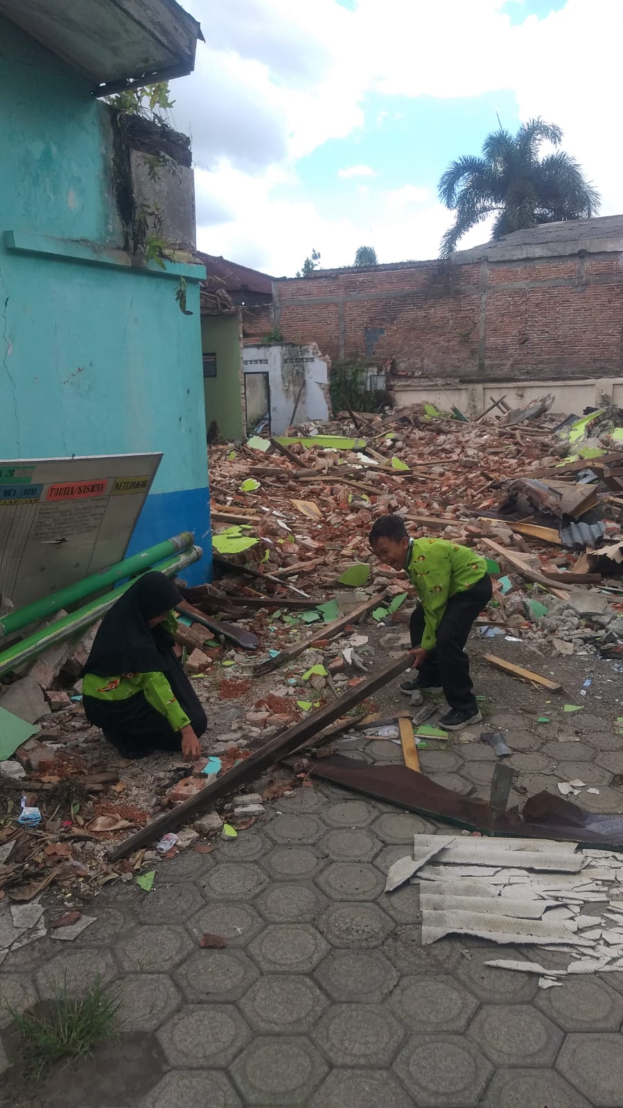 Dua siswa SDN Tlogo II tampak mengangkat kusen bekas eks Kantor UPTD Kanigoro yang dirobohkan kemarin (4/2). Keluh Kesah Warga SDN Tlogo II yang Bakal Kehilangan 3 Ruang Kelas