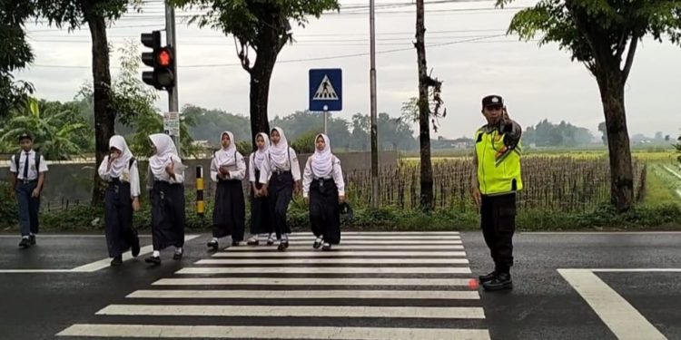 Personel Polsek Udanawu saat membantu siswa-siswi menyeberang jalan di wilayah Kecamatan Udanawu. &lrm; &lrm;Tekan Kecelakaan, Atur Lalu Lintas Jam Rawan