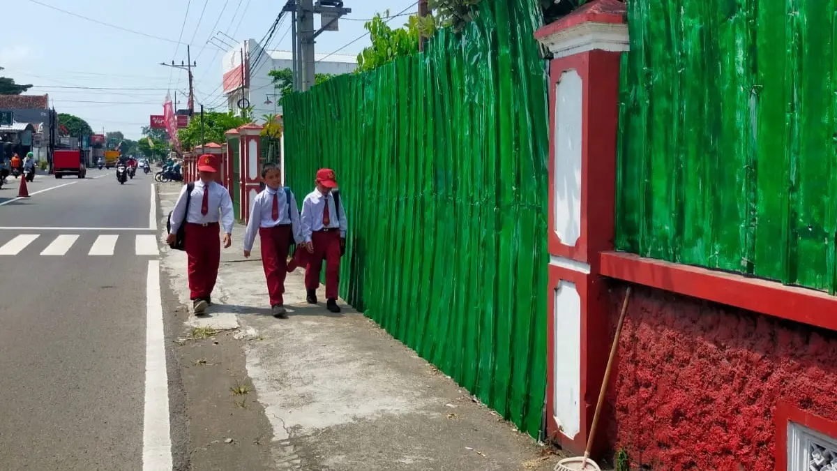 MIRIS: DUA SISWA SDN Tlogo 2 berjalan menyusuri pinggir tembok seng tempat pembangunan KDMP di samping sekolah
