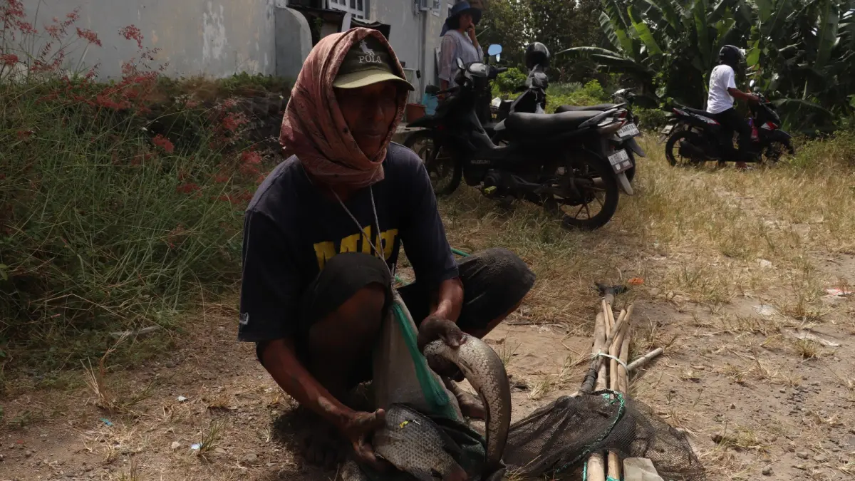 FAJAR RAHMAD ALI WARDANA/RADAR BLITAR - PANEN MUSIMAN: Sunarno menunjukkan sejumlah ikan hasil tangkapannya dekat area bendungan Wlingi Raya, Senin (18/5).