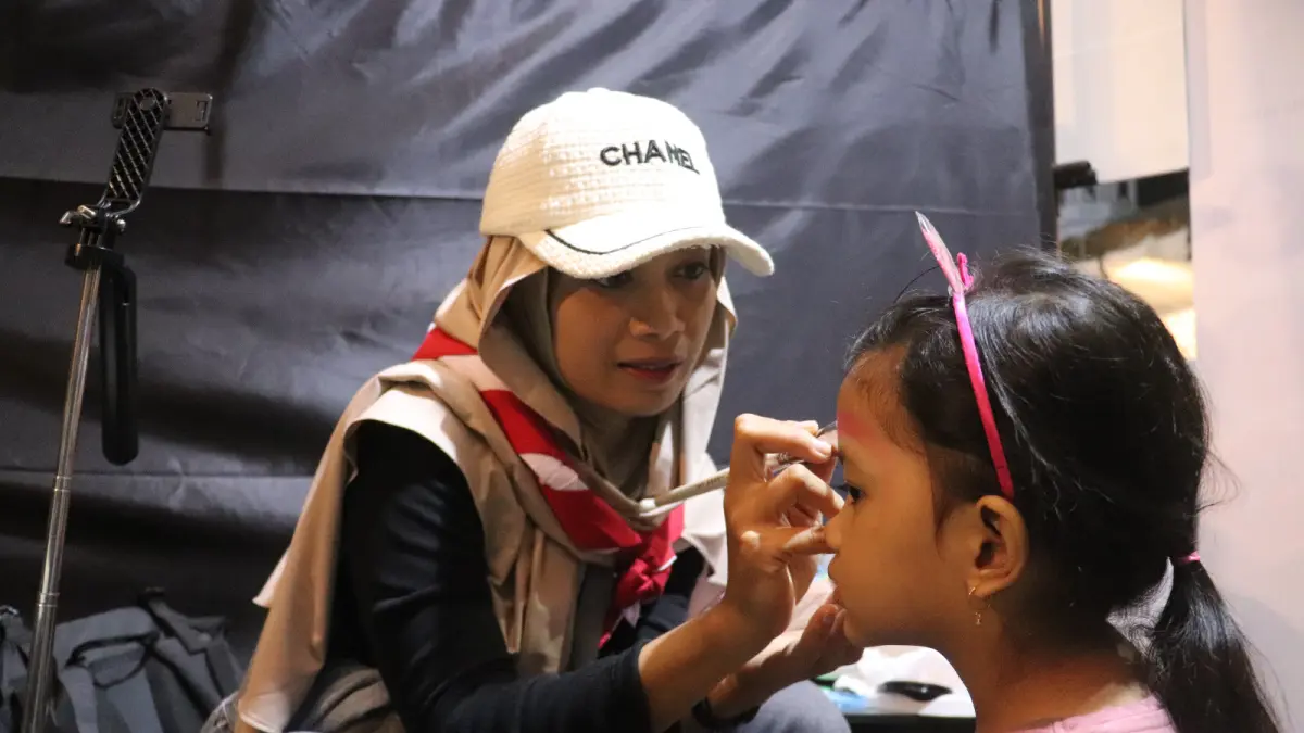 Intan Luvitasari merias wajah seorang anak dengan karakter lucu menggunakan cat khusus body painting. Jasa face painting miliknya kini menjadi daya tarik di berbagai keramaian di Blitar.
