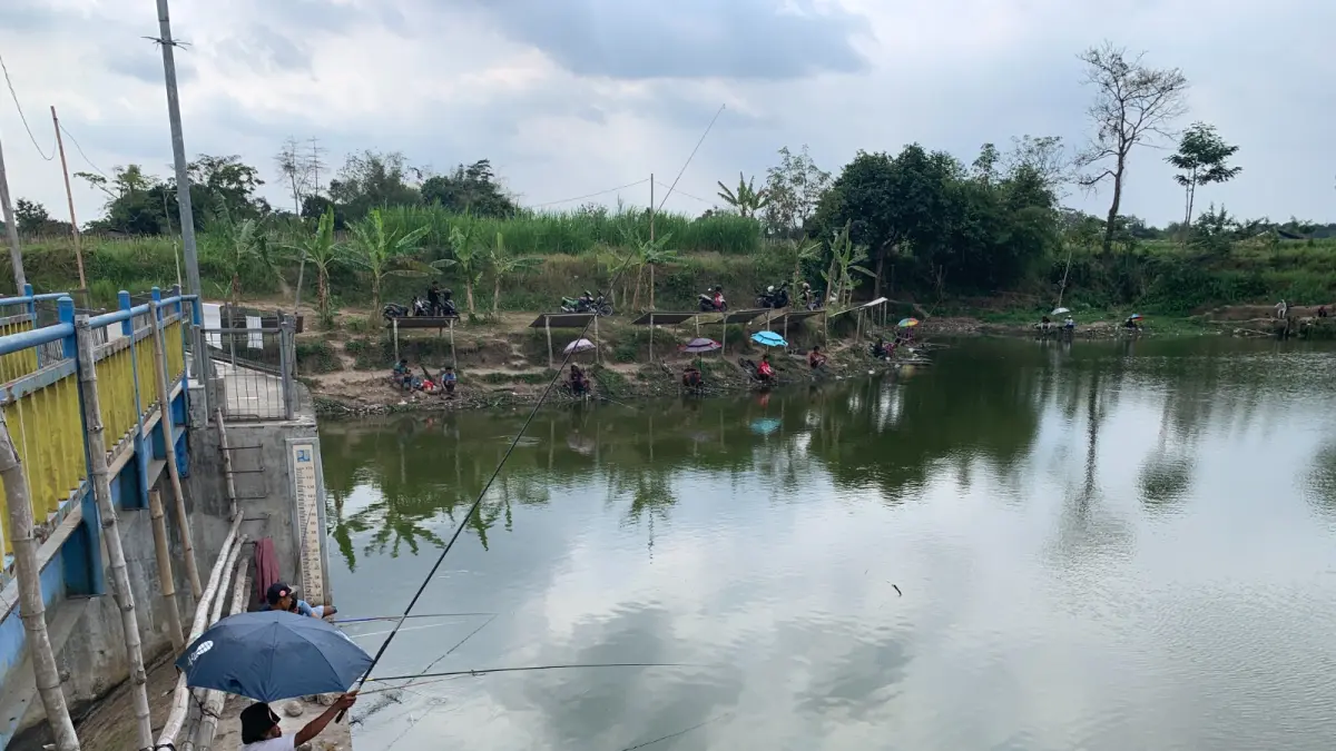 MOCH SUBCHAN ABDULLAH/RADAR BLITAR
DEMI HOBI: Pemancing bersantai di bawah pintu air Embung Jatimalang sembari menunggu sambaran umpan, kemarin (26/8). 
