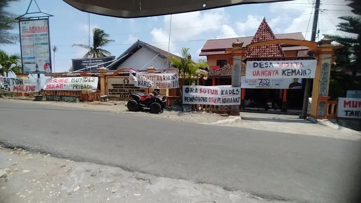 17 tuntutan warga Desa Serang dinilai belum tuntas. Spanduk “Turunkan Handoko” hingga kritik soal BUMDes mewarnai aksi di balai desa.