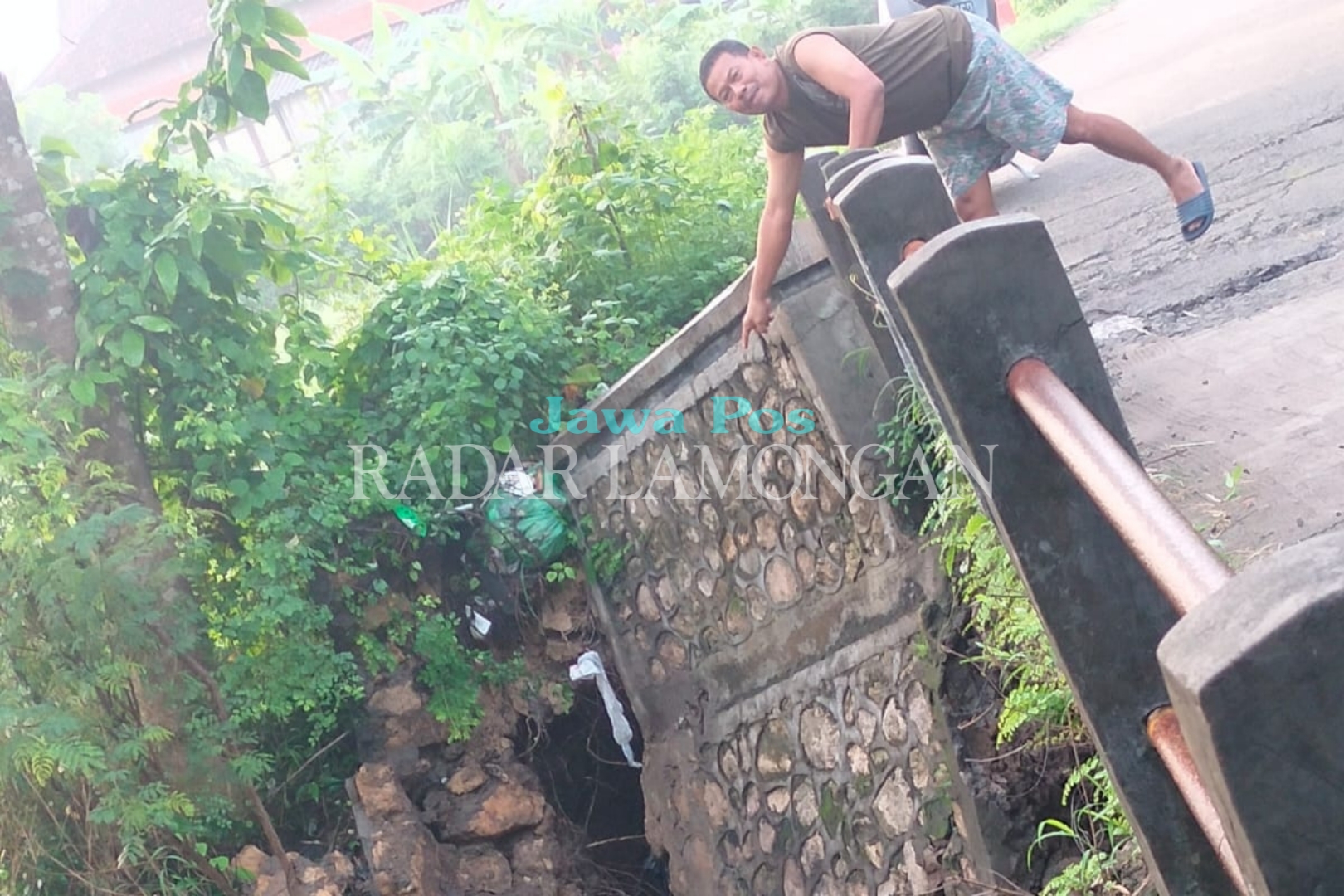 TERGERUS: Salah satu warga menunjukkan titip bawah jembatan di Desa Sidomulyo yang ambles. (Ist. / Radar Lamongan)