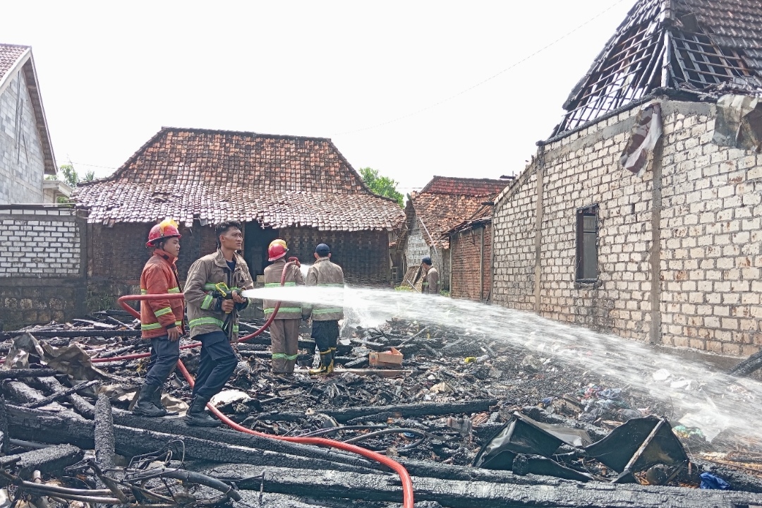TERSISA PUING-PUING: Petugas damkar saat menyemprotkan air di rumah Tarmudi. Tiga bangunan di sekitarnya terimbas kebakaran ringan. (Ist. / Radar Lamongan)