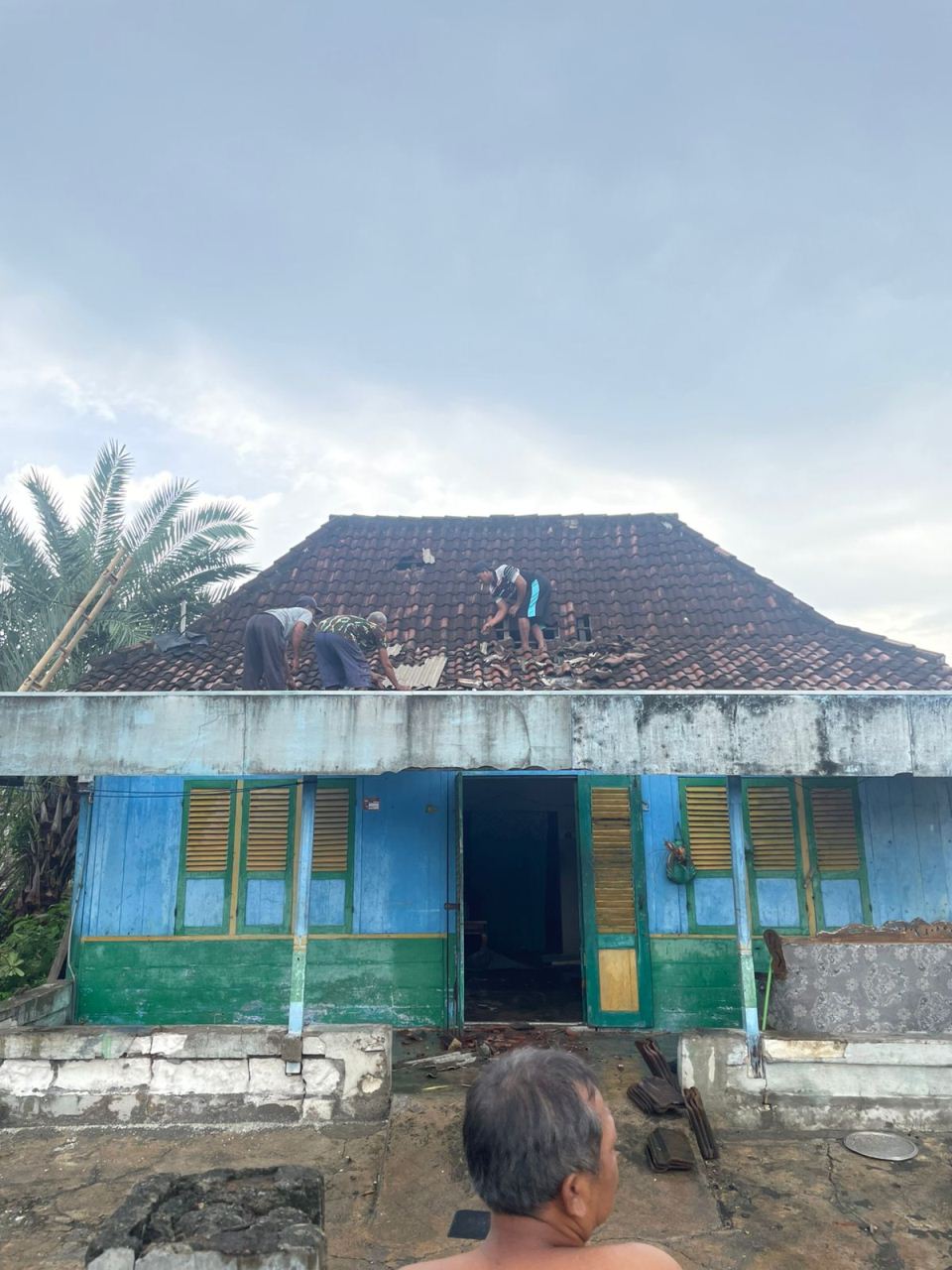 PERBAIKI ATAP RUMAH: Warga naik ke atas rumah untuk memperbaiki genting yang rusak akibat hujan disertai angin kencang. (IST/RDR.LMG)