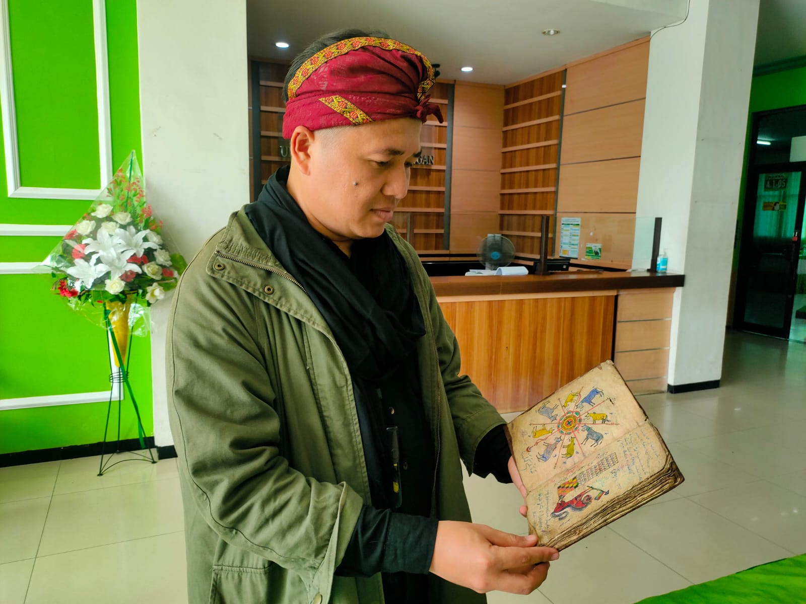 USANG: Diaz Nawaksara saat menunjukkan salah satu manuskrip primbon petangan lan naga dina, yang di dalamnya aksara pegon bahasa Jawa. ASIP A. / RADAR LAMONGAN