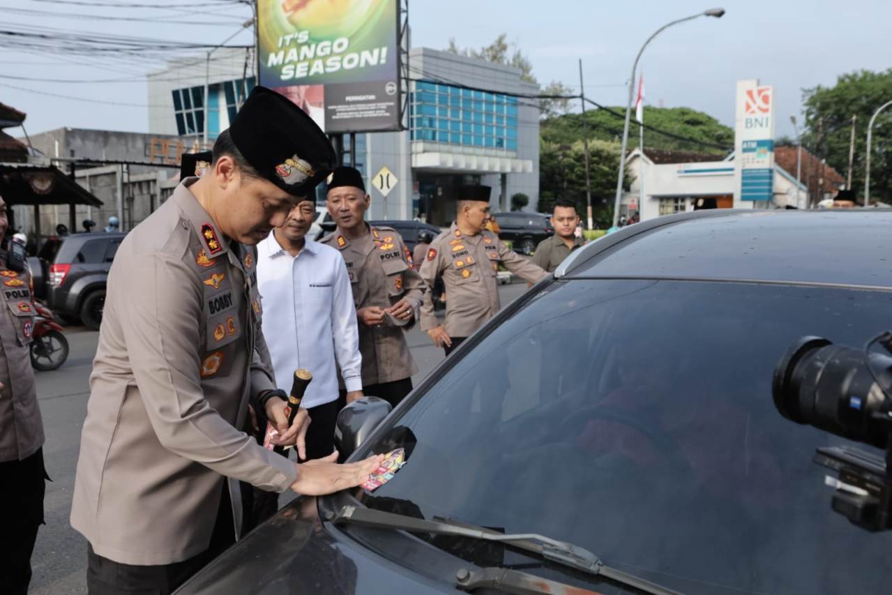 SOSIALISASIKAN HOTLINE: Kapolres Lamongan, AKBP Bobby A Condroputra, menempelkan stiker ke kaca mobil di jalan nasional. (IST/RDR.LMG)