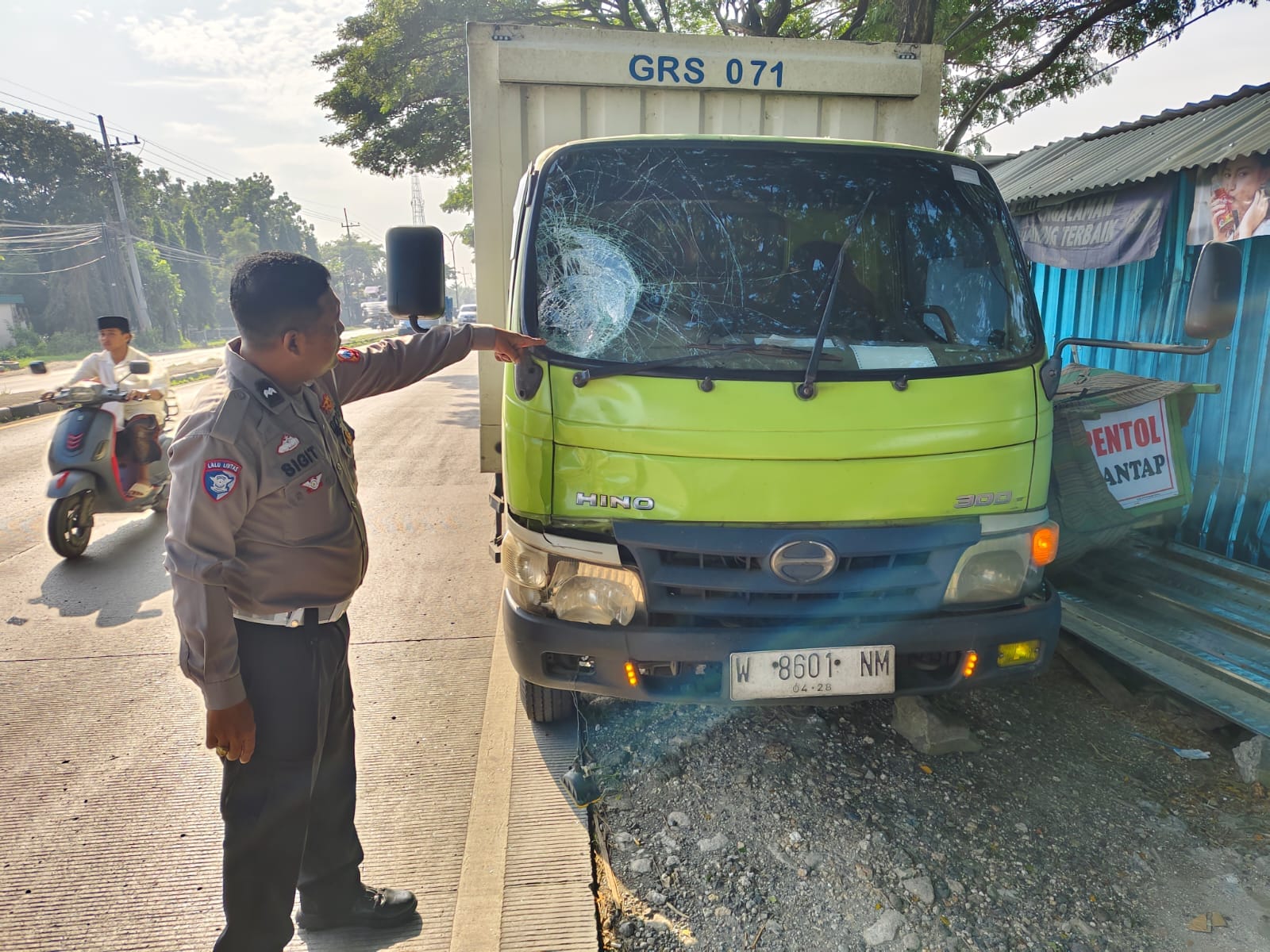 Petugas kepolisian menunjukkan kaca truk yang retak usai terlibat laka lantas di jalan nasional.
