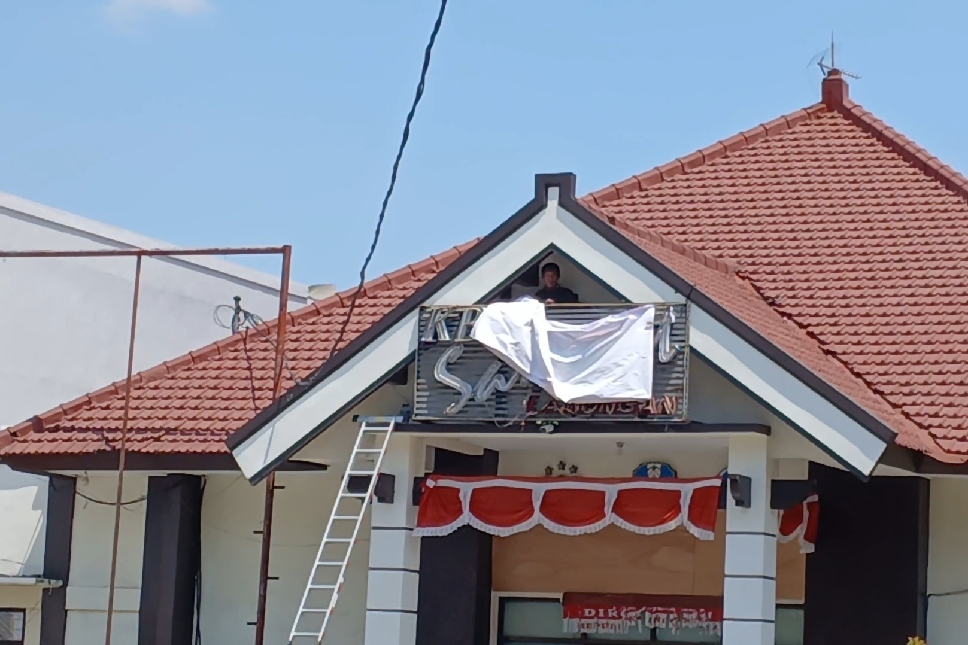 Petugas Kantor Bersama (KB) Samsat Lamongan menutup papan nama dengan benner.