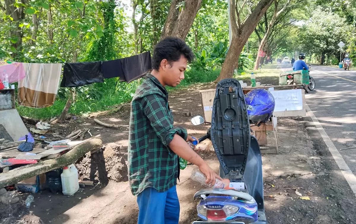 LAYANI PEMBELI - Agung saat melayani salah satu pembeli bensin di lapaknya yang sangat sederhana di jalur alas Roban Batang. (Lutfi Hanafi/RADAR SEMARANG)