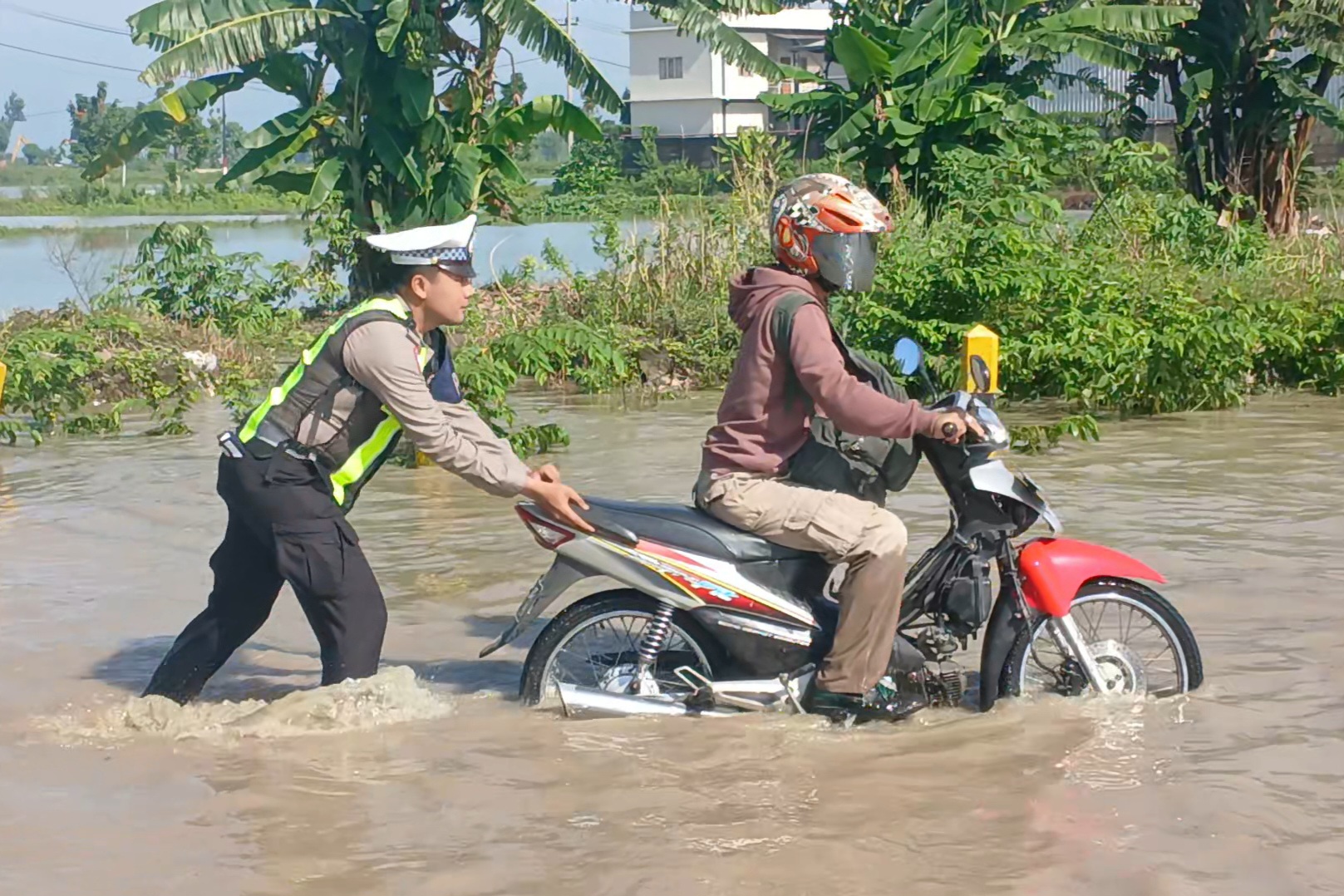 Petugas Satlantas Polres Lamongan membantu mendorong motor milik pengendara yang mogok karena melintas genangan air luapan Kali Plalangan.