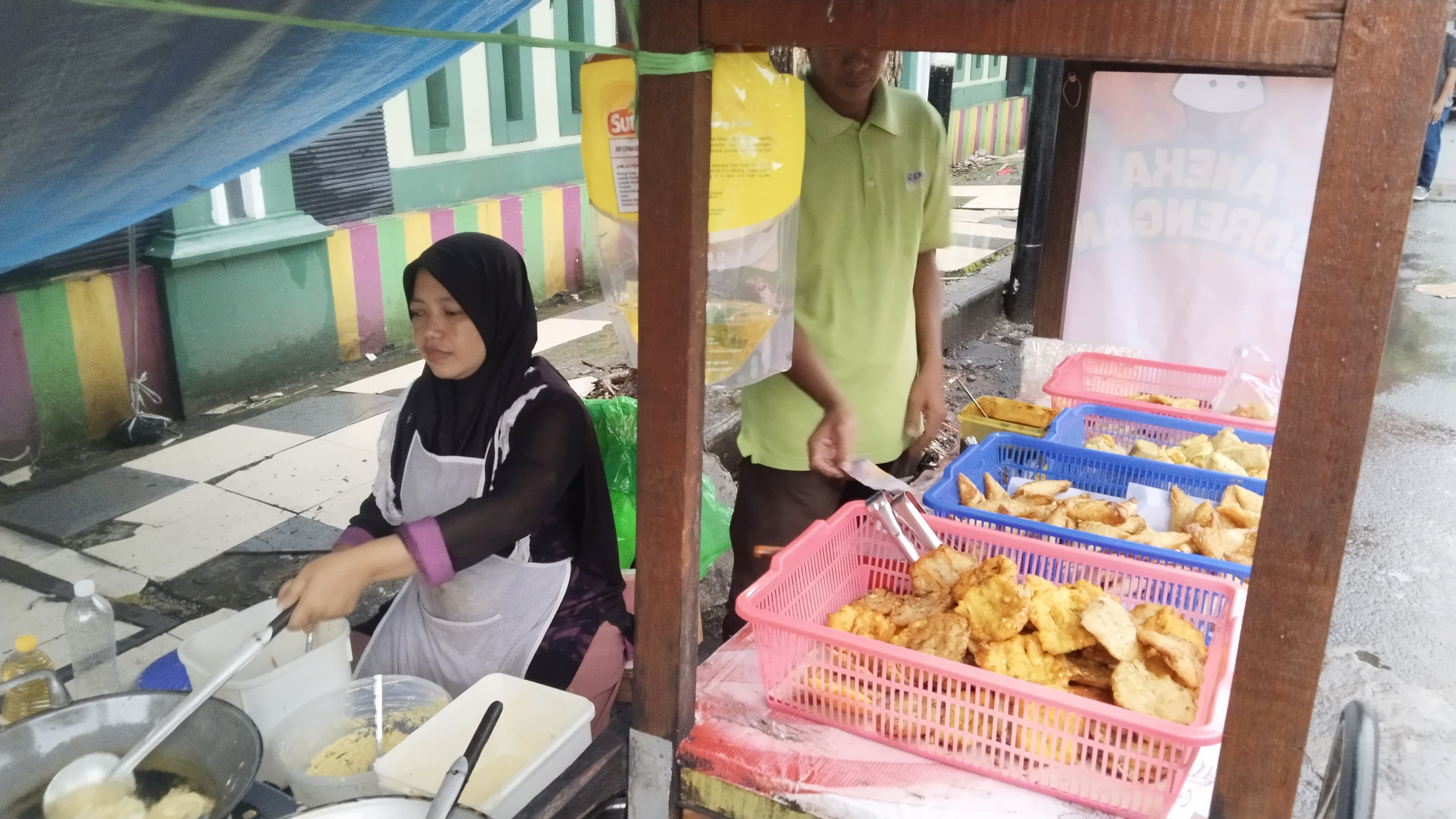 Pedagang yang menjajakan gorengan sepi pembeli saat hujan. 