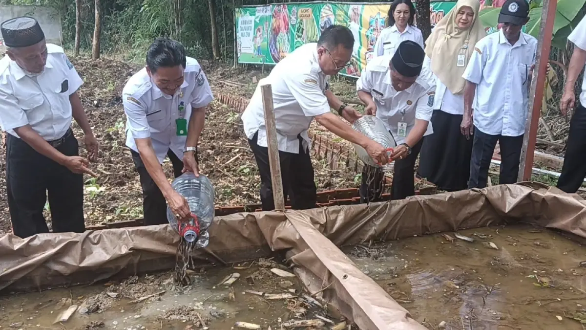 Kepala SMAN 1 Bluluk Muhtarom, S.Pd., M.Si., mendampingi Kacabdin Pendidikan Provinsi Jatim Wilayah Lamongan Dr. Budi Sulistyo, S.Pd. M.Si dalam penebaran bibit belut. (ISTIMEWA/RADAR LAMONGAN)