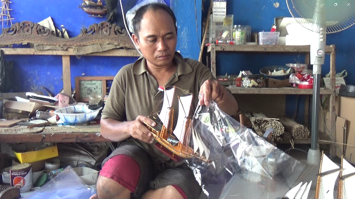 KREATIF: Sunali mengemas karya kerajinan miniatur kapal Majapahitan untuk dikirimkan ke pelanggan. (foto Reza for Radar Majapahit).