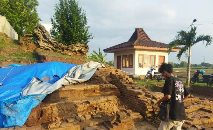 DALAM PENELITIAN: Pengunjung mengamati bagian depan bentuk Candi Watesumpak, di Desa Watesumpak, Kecamatan Trowulan, yang ditutup menggunakan terpal. (foto M. Khasib for Radar Majapahit)