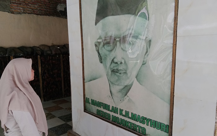 ULAMA: Peziarah memandang foto Kiai Masyhuri berukuran besar. Semasa hidup Kiai Masyhuri dikenal seorang tokoh agama yang disegani masyarakat sekitar. (foto: Bryan Noer for Radar Majapahit).