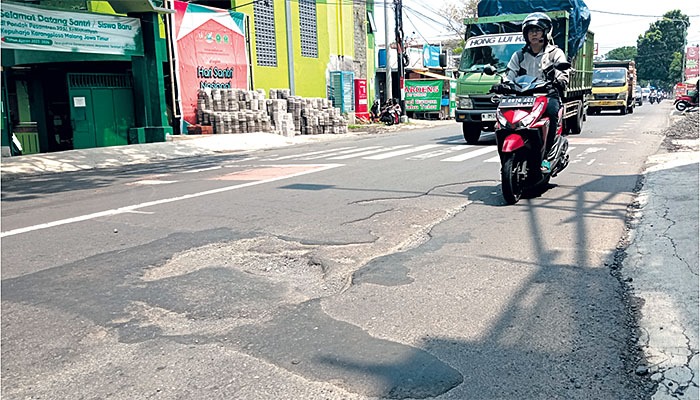 RAWAN KECELAKAAN: Pengendara melintas di dekat spot jalan rusak dan berlubang di kawasan Desa Kepuharjo, Kecamatan Karangploso