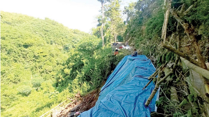 SEGERA DITANGANI: Petugas memasang terpal di lokasi jalan yang longsor di Jalan Rajekwesi, Kecamatan Kalipare, Kabupaten Malang.