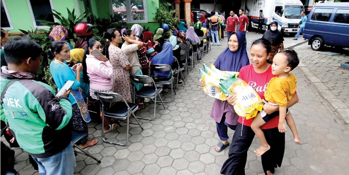 MAKSIMAL DUA KANTONG: Ibu-ibu membawa beras di dekat antrean warga yang menunggu giliran membeli beras murah di halaman kantor Dinas Ketahanan Pangan Kabupaten Malang kemarin (1/3).
