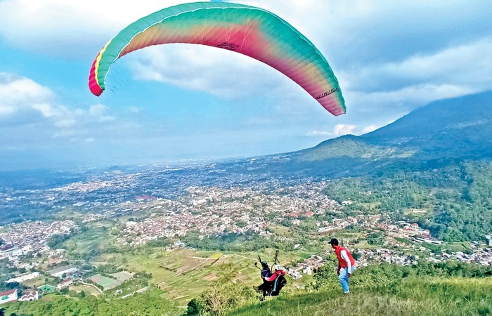 MENEGANGKAN: Salah seorang wisatawan melakukan take off paralayang didampingi pilot tandem di Gunung Banyak, Kecamatan Batu beberapa waktu lalu.