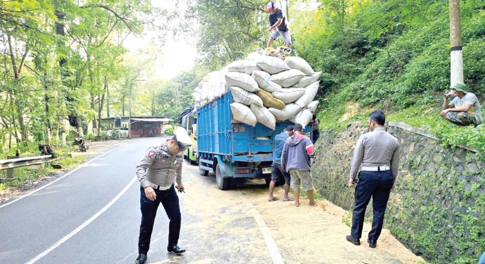 PROSES EVAKUASI: Truk warna biru yang mengangkut sekam berhasil berdiri kembali setelah terguling di Jalan Trunojoyo, Desa Songgokerto, Kecamatan Batu kemarin. SATLANTAS POLRES BATU FOR RADAR BATU