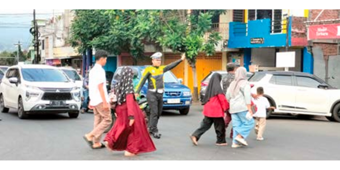 OPERASI KETUPAT SEMERU: Salah seorang petugas Polres Batu sedang membantu sejumlah warga menyeberang di Jalan Diponegoro beberapa waktu lalu.