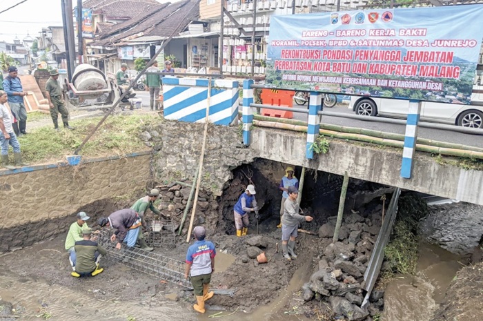 GOTONG ROYONG: Para warga dan aparat penegak hukum sedang melakukan rekontruksi pondasi penyangga jembatan perbatasan Kota Batu dan Kabupaten Malang kemarin (22/6).