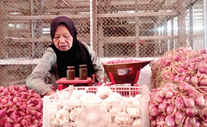 MELAYANI PEMBELI: Salah seorang pedagang bawang merah di Pasar Sayur Kota Batu menimbang bawang merah yang harganya tembus Rp 55 ribu per kilogram kemarin (24/7).