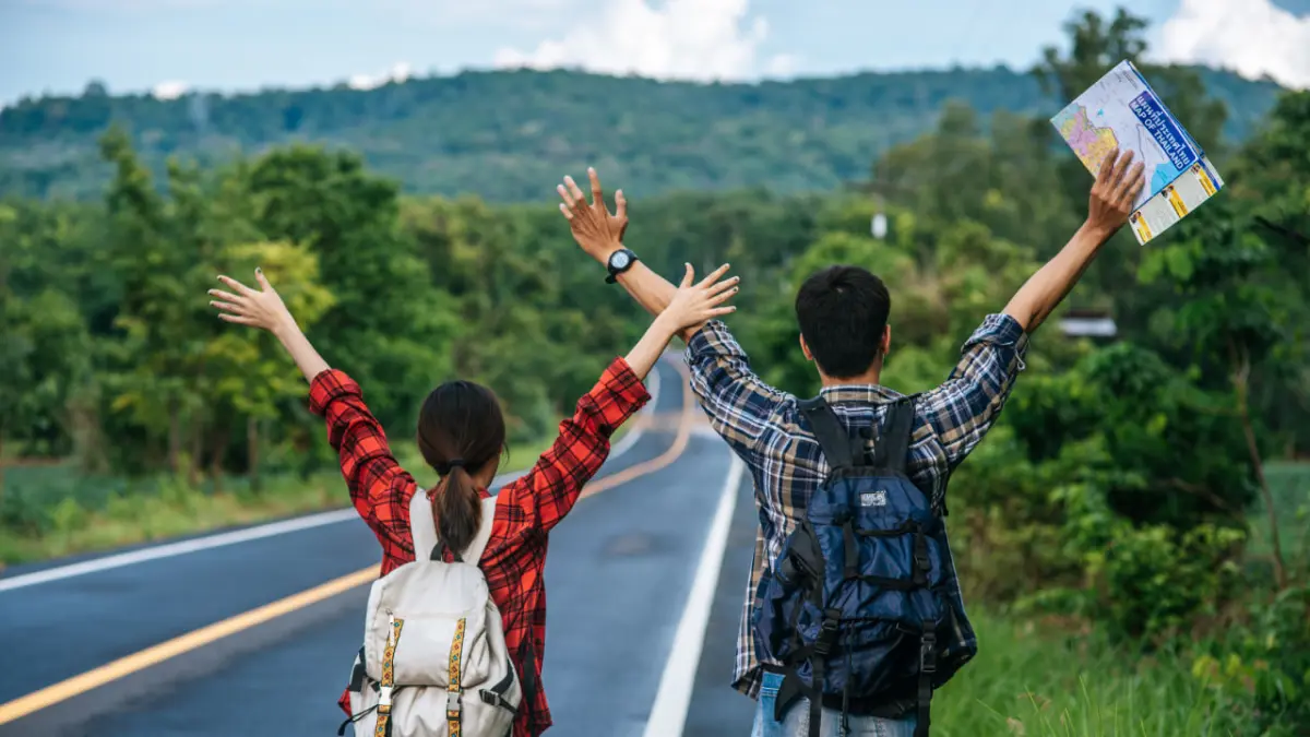 Dua turis sedang menunggu transportasi di pinggir jalan. (Sumber: Freepik)

