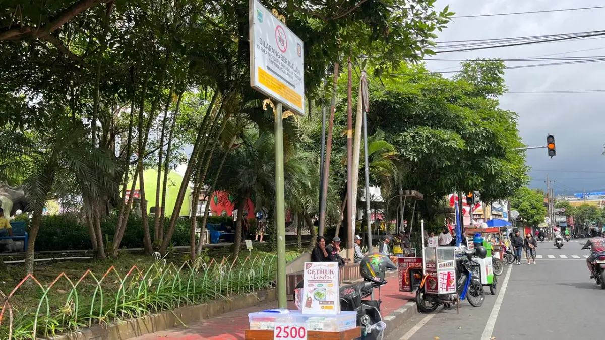 PEDAGANG MUSIMAN: Seorang PKL liar di sekitar Alun-Alun Kota Batu nekat menggelar lapak persis di bawah plakat bertuliskan “DILARANG BERJUALAN” kemarin (17/5).