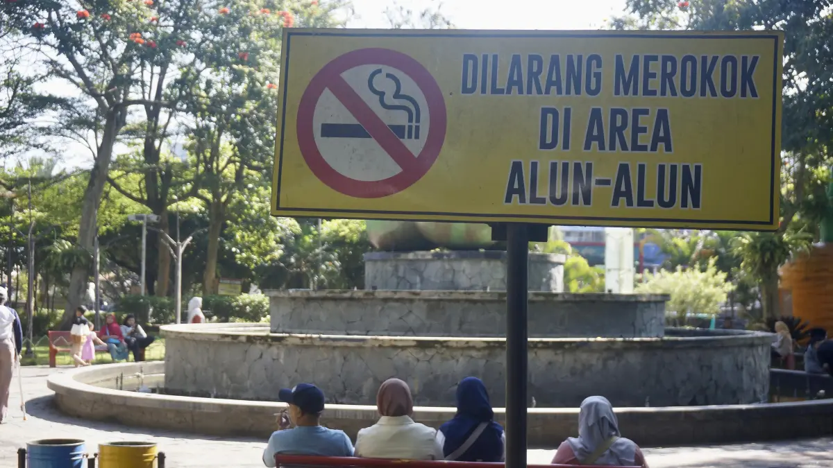 DILARANG MEROKOK: Salah seorang pengunjung Alun-Alun Kota Batu merokok di dekat rambu edukasi kawasan tanpa rokok (KTR) beberapa hari lalu.