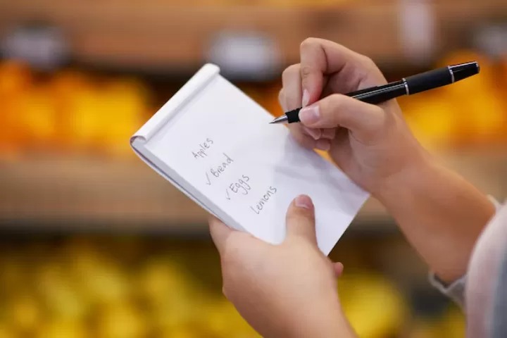 Seseorang yang menulis daftar belanja di kertas.