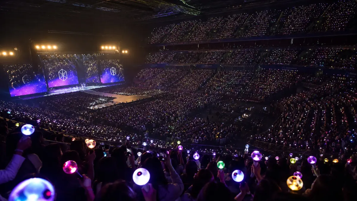 Ilustrasi suasana konser K-pop dengan ribuan lightstick yang menyala memenuhi arena, menciptakan lautan cahaya yang menjadi ciri khas pertunjukan. (AI Generated)