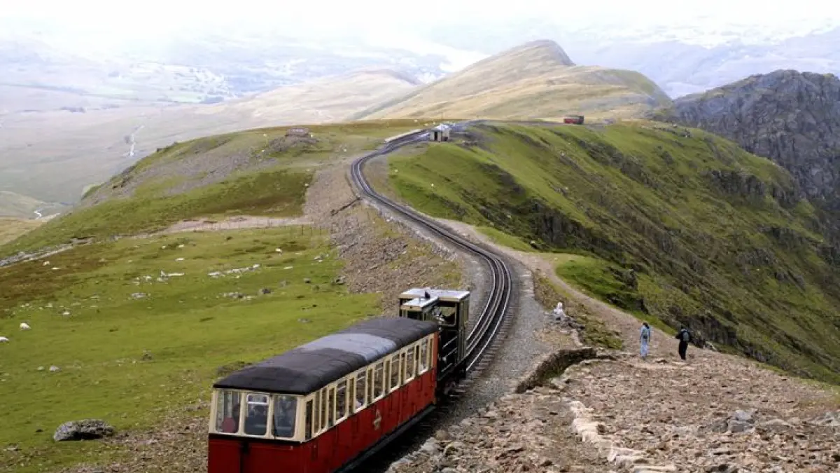 Bukan kereta biasa! Snowdon Mountain Railway membawa penumpang mendaki Yr Wyddfa, gunung tertinggi di Wales. Dengan sistem rel bergigi, kereta ini mampu menaklukkan jalur yang sangat curam hingga lebih dari 1.000 meter. (Pinterest)