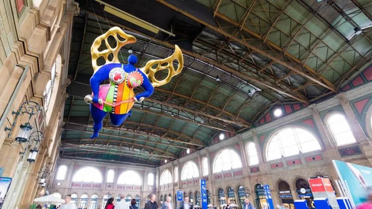 Di tengah kesibukan Zürich Hauptbahnhof, ada satu sosok yang justru membuat orang berhenti dan menengadah. “Nana”, karya Niki de Saint Phalle, menggantung di aula utama stasiun dan menjadi salah satu ikonnya. (Pinterest)