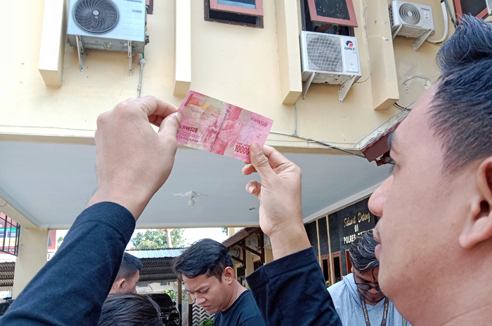 CETAKAN KASAR: Anggota Satreskrim Polres Rembang menerawang lembaran uang palsu pecahan Rp 100 ribu yang diamankan dari pelaku.