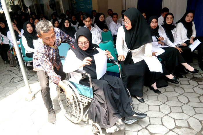 DIDORONG: Personel BKD Rembang mendorong kursi roda Budi Hestina, peserta seleksi PPPK pasca melahirkan ke tempat registrasi, Senin (13/11).