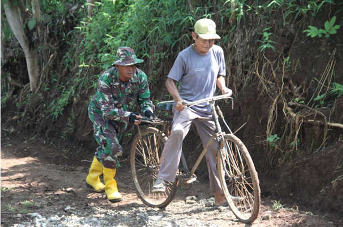 SIGAP : Seorang anggota TNI mendorong sepeda yang dinaiki warga saat melintas di jalanan yang terjal di Desa Tanjungrejo Kecamatan Margoyoso Pati.