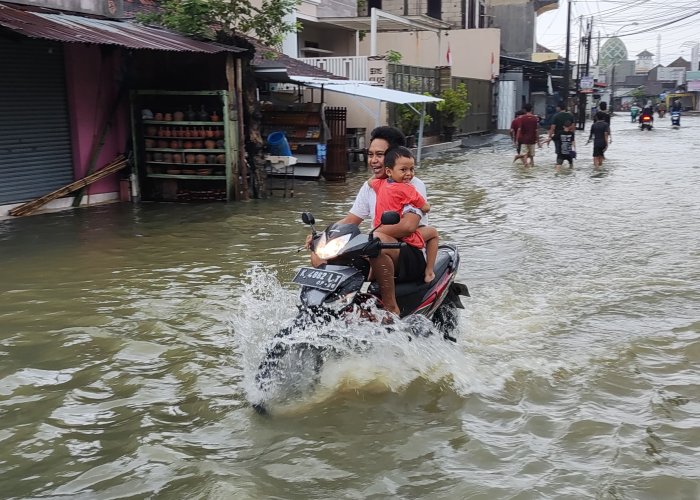 WASPADA: Warga sedang melintas di perempatan Mejobo yang terdampak banjir pada Kamis (14/3).