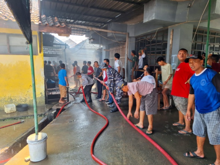 TERBAKAR: Warga bersama petugas damkar memegang selang air di Gudang fiber di TPI I Juwana.