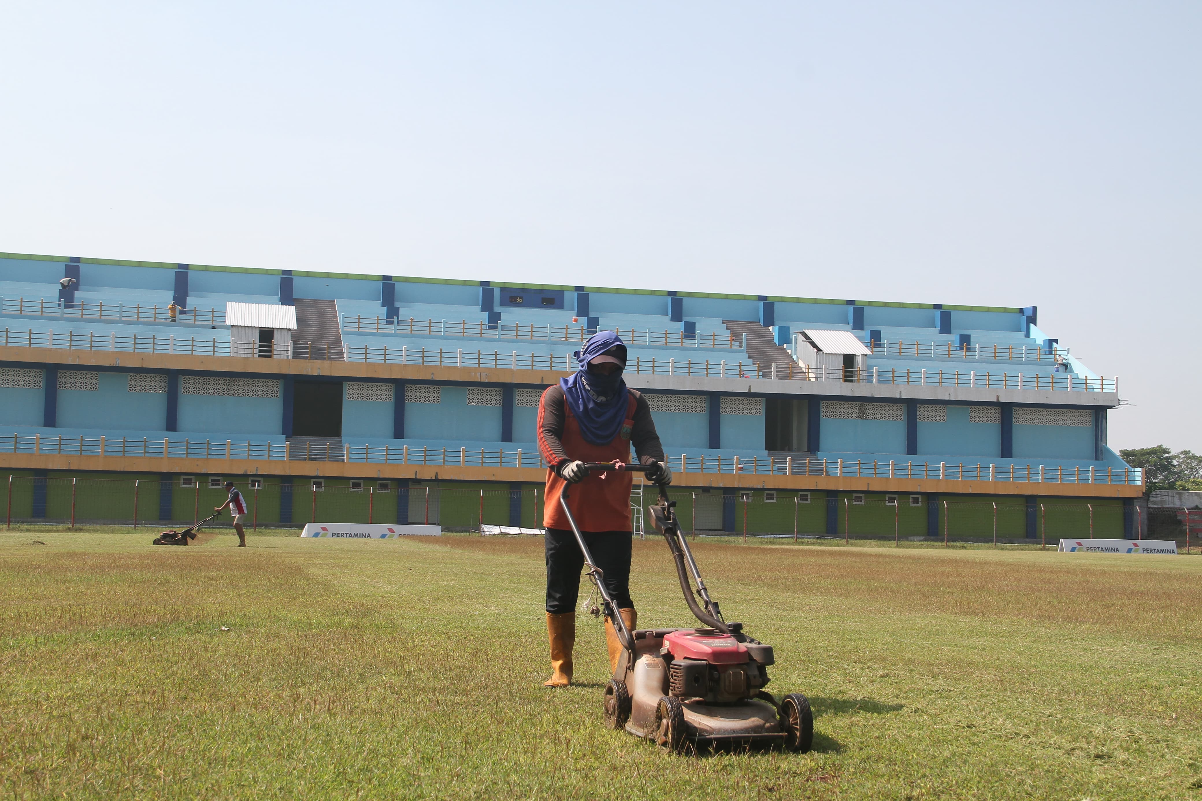 DIKEBUT: Pekerja sedang memotong rumput lapangan Stadion Wergu Wetan. Sedangkan tribun stadion sudah selesai dicat biru.