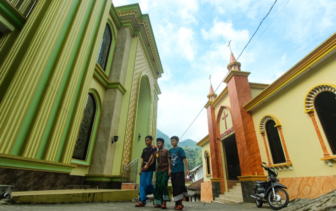 RUKUN: Masyarakat melintas di depan sebuah masjid dan gereja yang saling berhadapan di Desa Tempur.