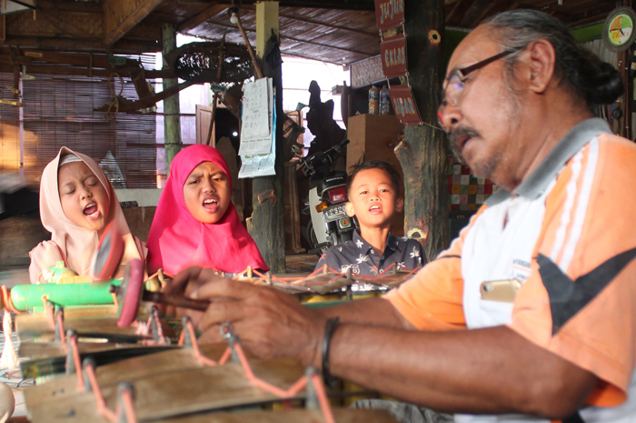 URI-URI BUDAYA: Suyadi alias Pak Raden memainkan alat musik gender, sementara anak-anak latihan mocopat di Padepokan Adhem Ayom Ayem, Desa Godan, Tawangharjo, Grobogan, belum lama ini.