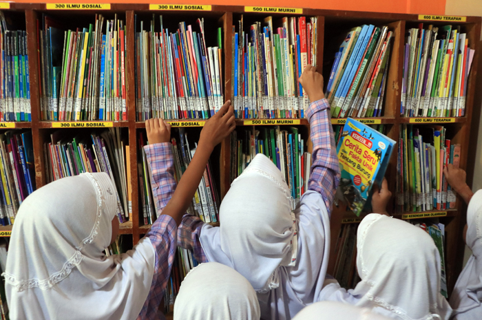 MEMBACA: Anak-anak serius dan enjoy saat membaca buku yang disediakan Perpustakaan keliling.